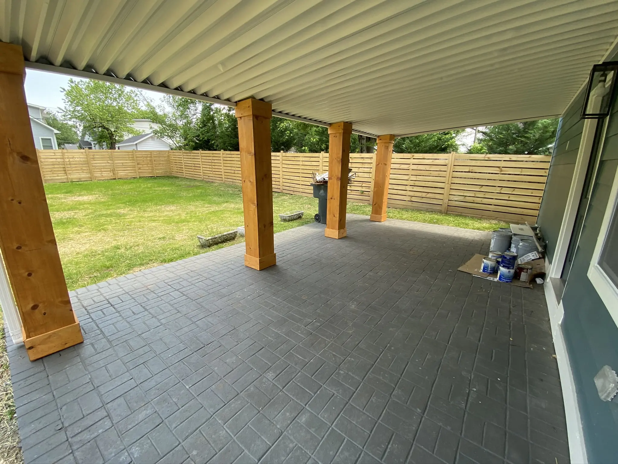 a covered patio area with a grill and a trash can
