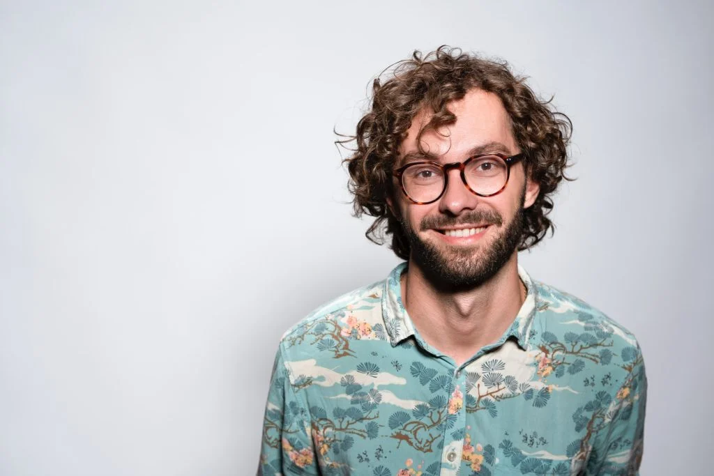 a man with curly hair and glasses is wearing a floral shirt