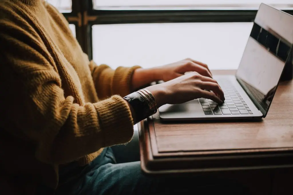 a person in a yellow sweater is typing on a laptop