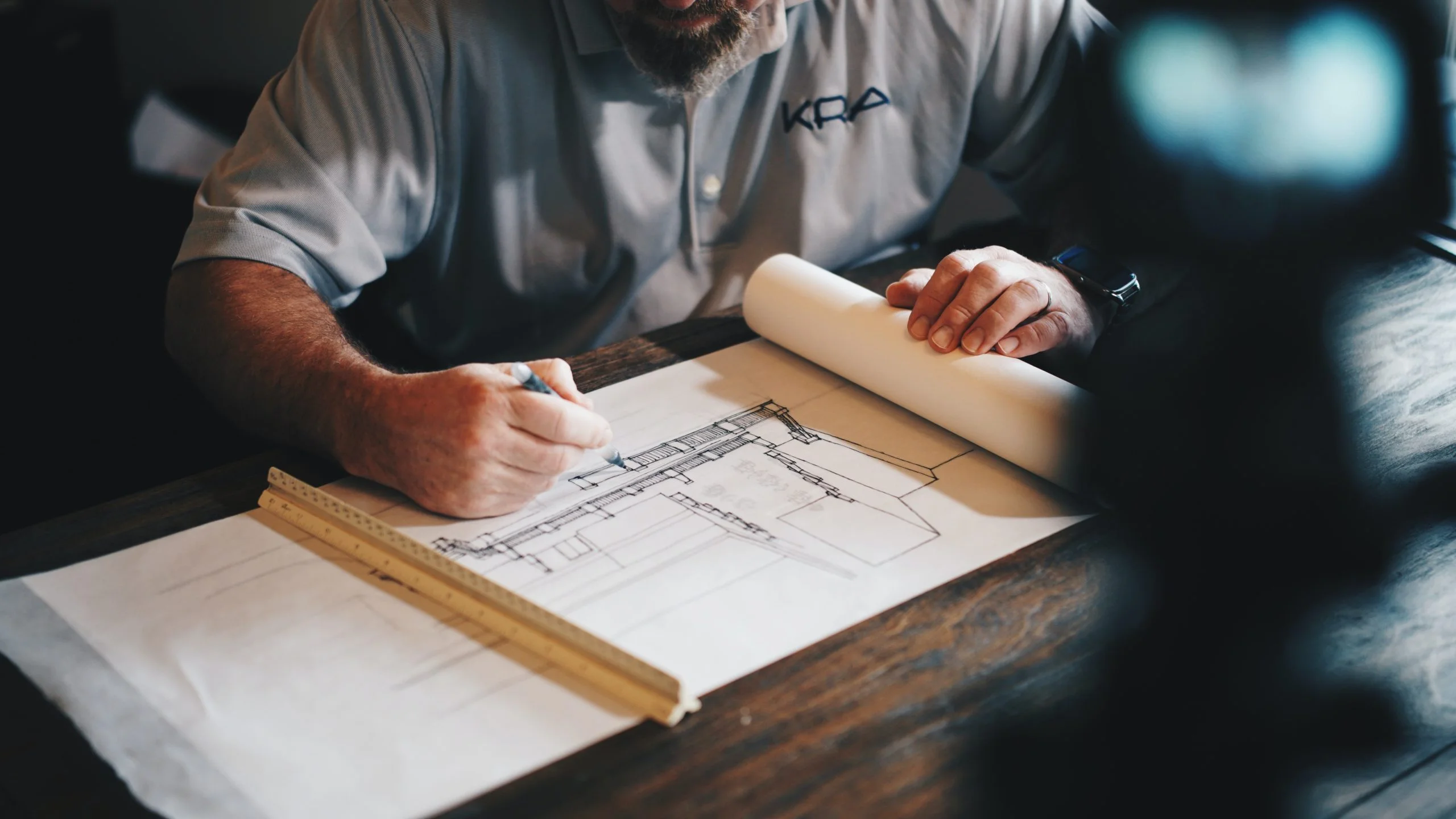 a man wearing a kra shirt is working on a blueprint