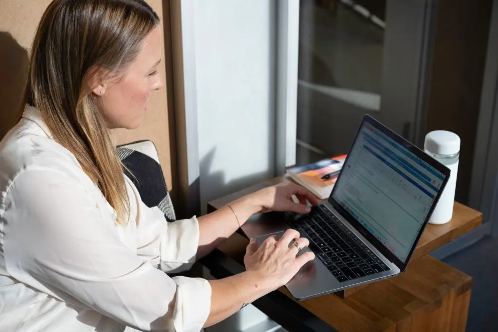 a woman in a white shirt is typing on a laptop