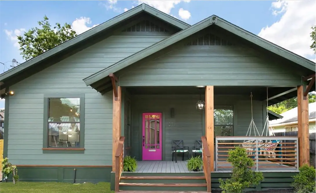 a green house with a pink door and porch