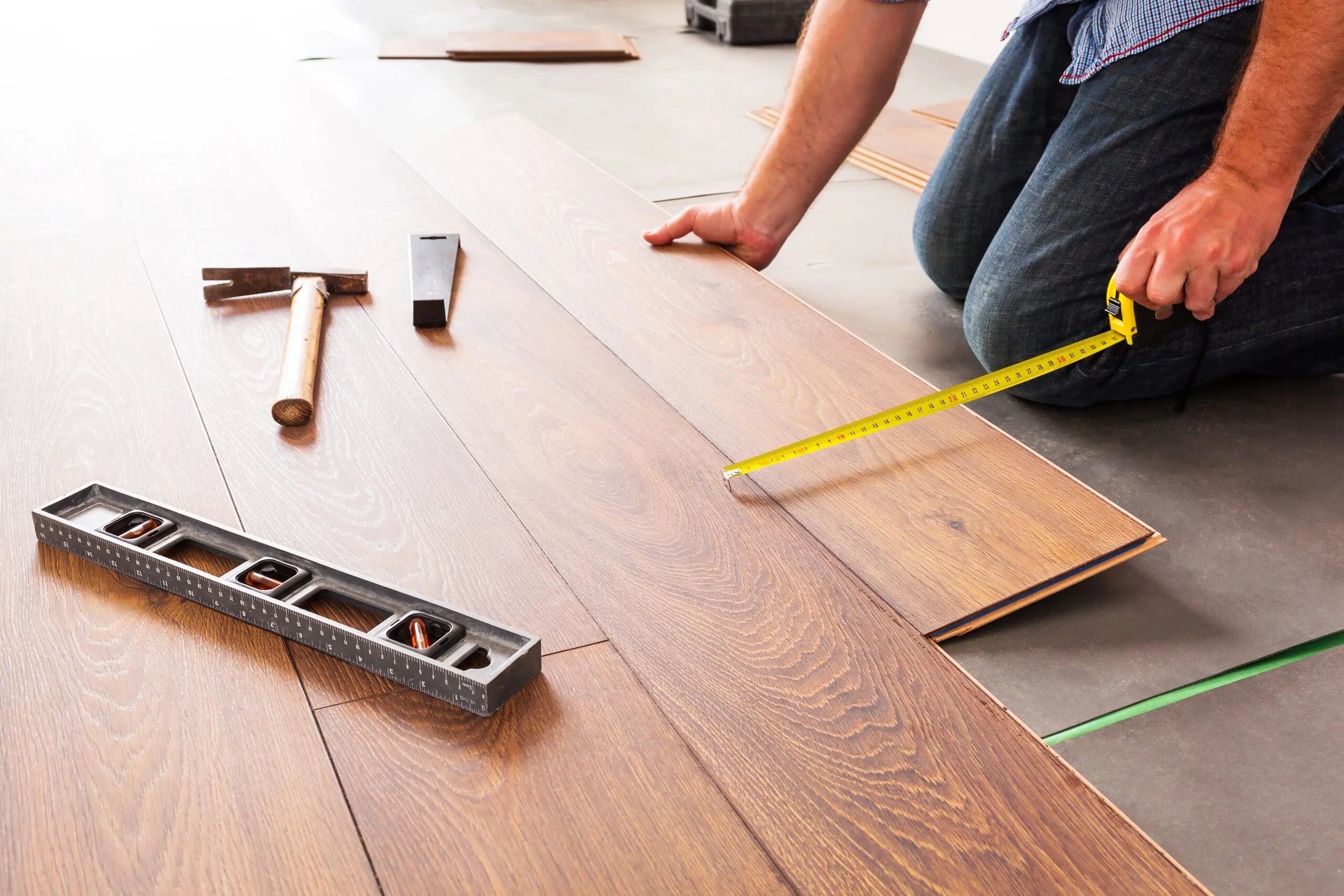 a man measuring a wooden floor with a tape measure
