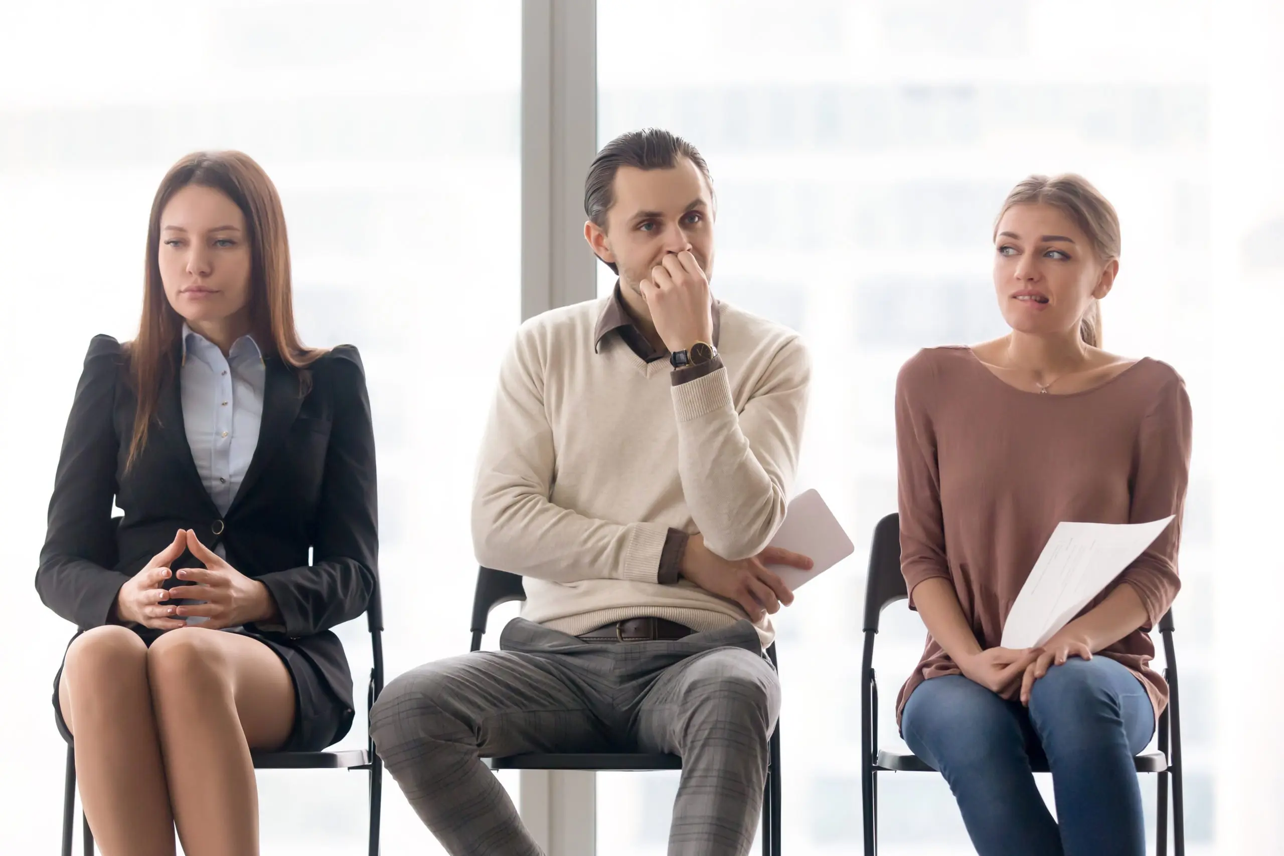 three people are sitting in chairs waiting for a job interview