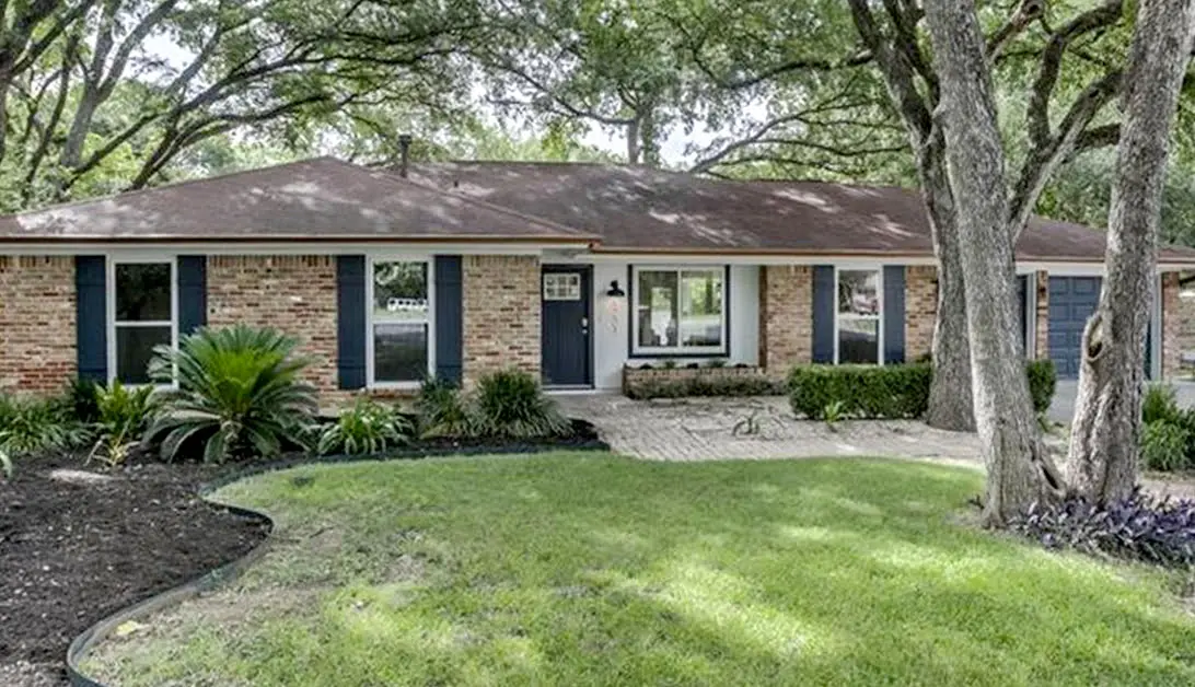 a brick house with blue shutters and trees in front of it