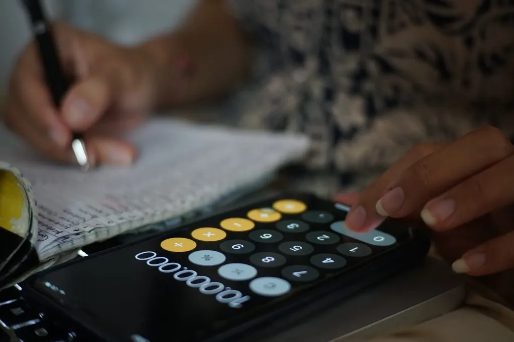 Cropped view of person writing on notepad and using a phone calculator