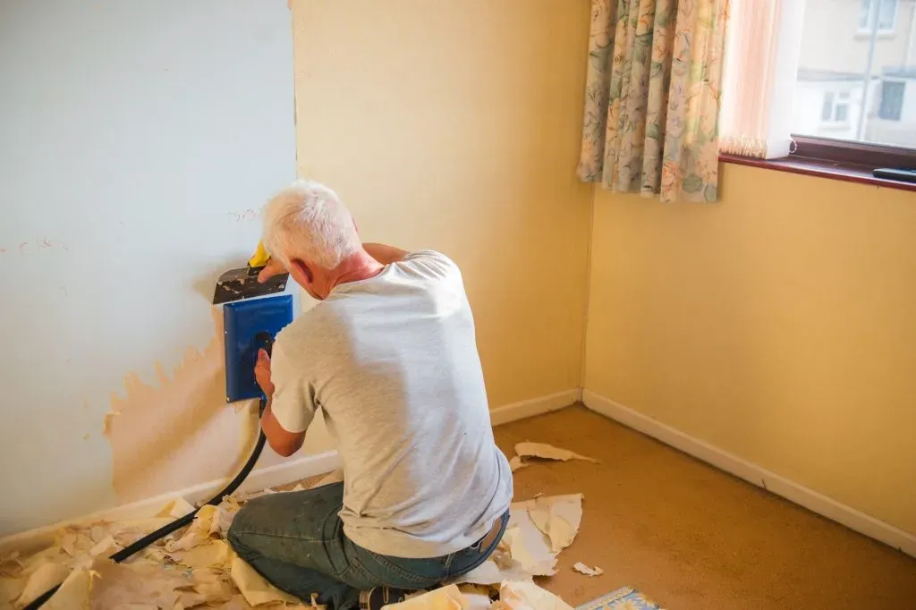 a-man-removes-old-wallpaper-from-a-wall-using-special-tools