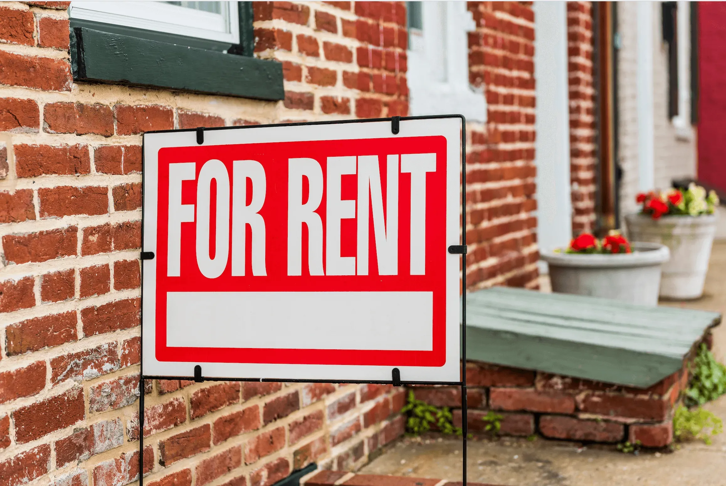 a red and white for rent sign next to a brick building