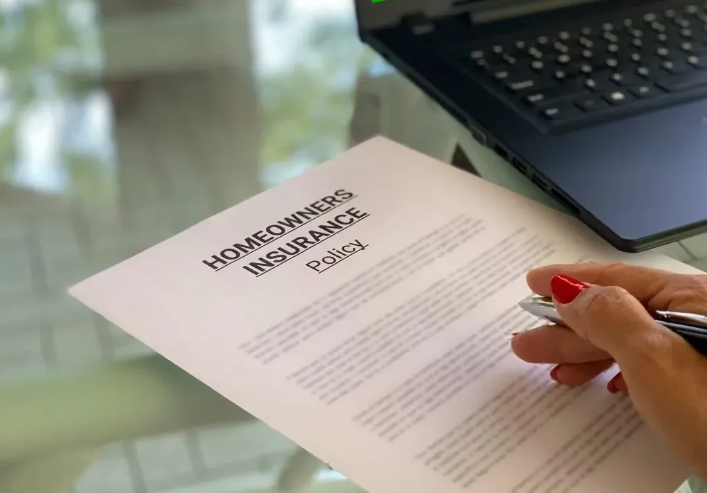 woman in workspace with laptop, homeowners insurance policy on desk
