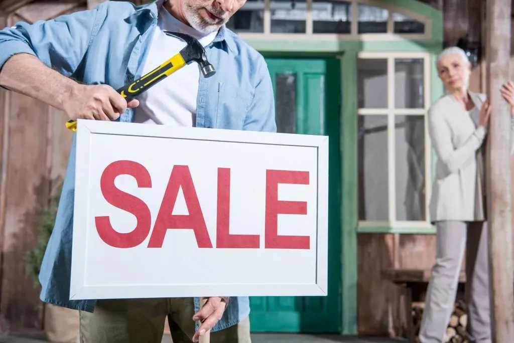 close-up-of-sale-sign-senior-couple-selling-their-home
